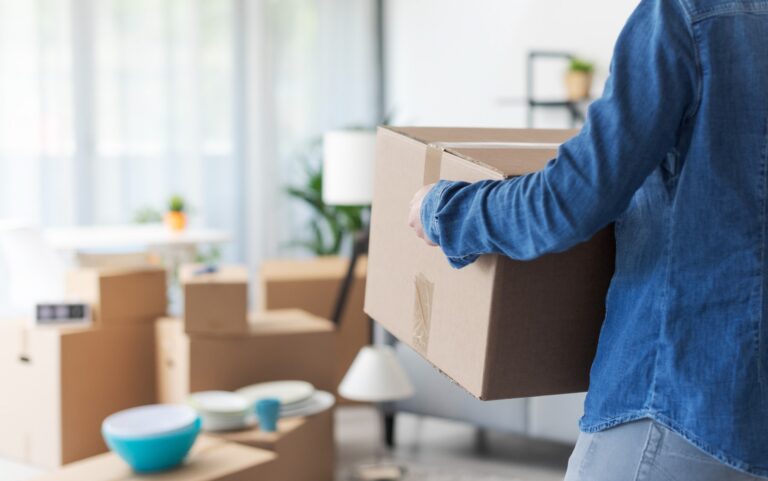 Person carrying a cardboard box into a new home on moving day.